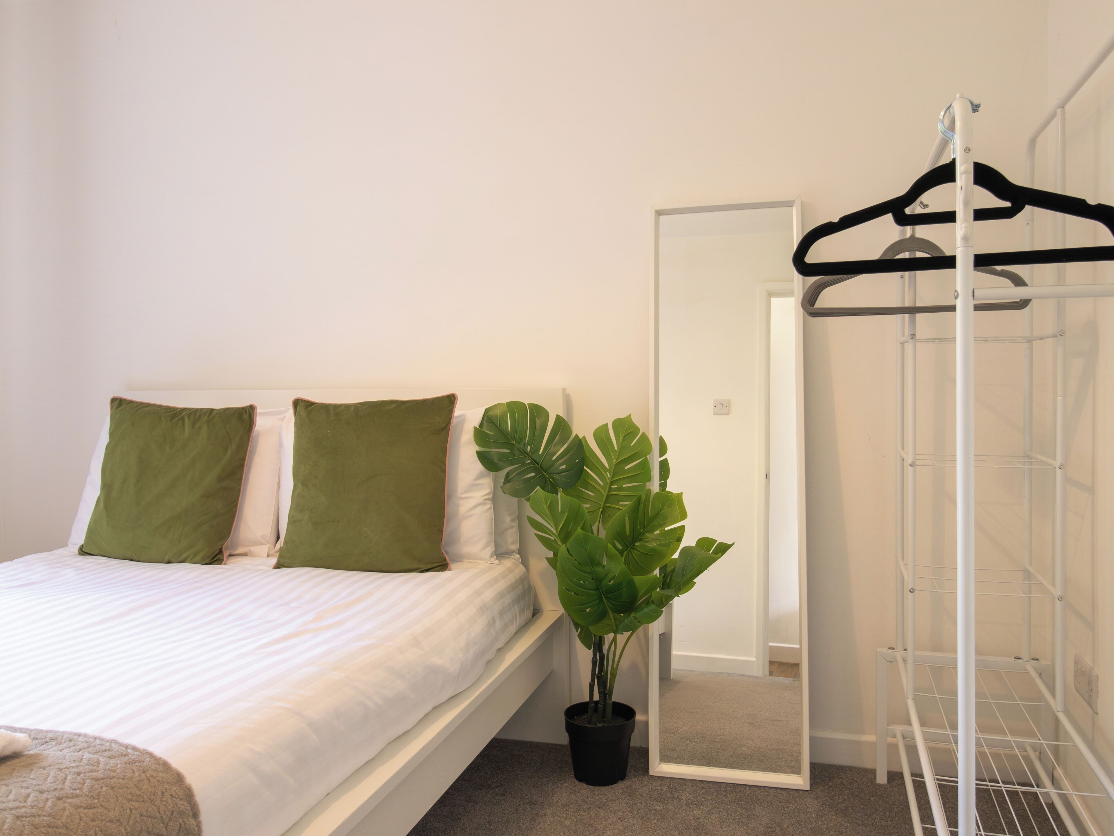 A neatly made bed with two pillows, a potted plant, and a white metal wardrobe.
