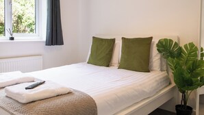 Ein Schlafzimmer mit einem Bett, Kissen, einer Fernbedienung, einer Decke, einem Fenster und einer Topfpflanze.