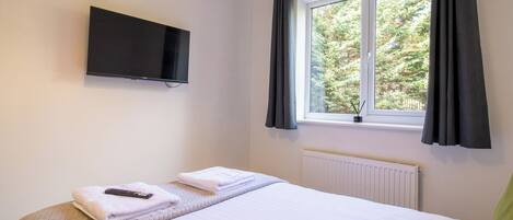 A bedroom with a bed, a TV mounted on the wall, a window with curtains, and a radiator.