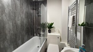 Un baño moderno con bañera, inodoro, lavamanos y ducha con mampara de vidrio.