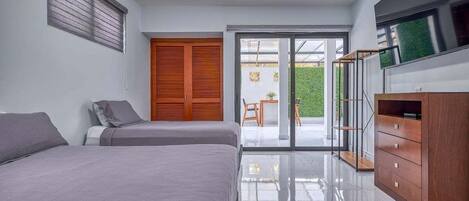 Un dormitorio moderno con dos camas, un armario de madera y un ventanal corredero que da a un balcón.