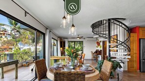 Ein Essbereich mit Korbstühlen und einem runden Tisch, gedeckt für vier Personen, eine Wendeltreppe und Blick ins Freie.