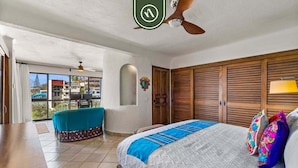 Ein Hotelzimmer mit einem Bett, einem Deckenventilator, einem Holzschrank und Blick durch eine Glastür nach draußen.