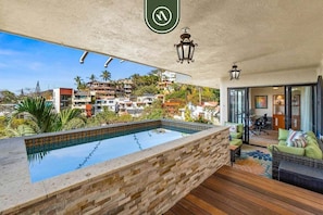 A rooftop pool with a stone wall, wooden deck, and outdoor seating area.