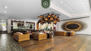 Een ruime lobby met een houten vloer, rieten meubels en een groot kunstwerk aan de muur.