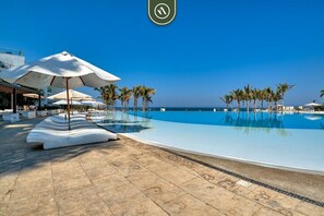 A poolside area with lounge chairs and umbrellas, palm trees, and a clear view of the ocean.