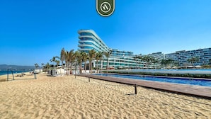 Un hôtel situé en bord de mer, doté d’une piscine, de palmiers et surplombant un ciel bleu azur.