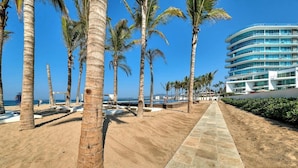 A beachfront hotel with palm trees, a sandy walkway, and a clear view of the ocean. - Aria Ocean 179 | 1BR, Nuevo Vallarta, pool & beach (Nuevo Vallarta)