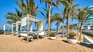 A beach with white lounge chairs and a palm tree. - Aria Ocean 179 | 1BR, Nuevo Vallarta, pool & beach (Nuevo Vallarta)