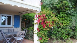 An outdoor patio with a table and chairs, surrounded by lush greenery and flowering plants. - Apartment CLIMATISE 4 persons (les  issambres)