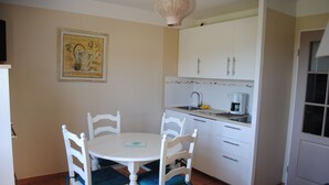 A compact kitchen with white cabinets, a sink, and a coffee maker. There is a dining table with chairs in the foreground. - Apartment CLIMATISE 4 persons (les  issambres)