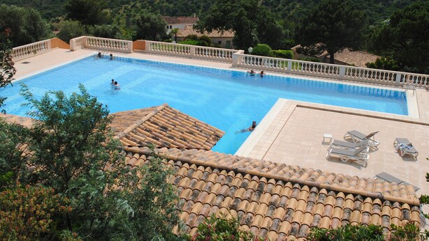 A swimming pool with tiled edges, surrounded by a white fence, and overlooking a hilly landscape with trees and buildings. - Apartment CLIMATISE 4 persons (les  issambres)