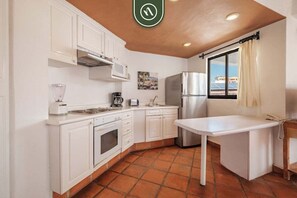 Cozinha com armários brancos, geladeira de aço inoxidável, cafeteira e janela com vista.