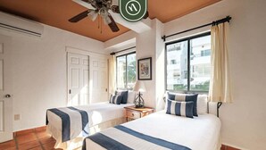 A hotel room with two beds, a ceiling fan, a window with curtains, and a door.