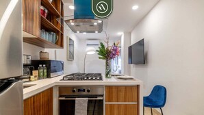 Una cocina compacta con horno integrado, cocina a gas, armarios de madera y una silla azul.