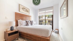 Un dormitorio moderno con cama de madera, una mesita de noche, una lámpara y un amplio ventanal con vistas a un balcón.
