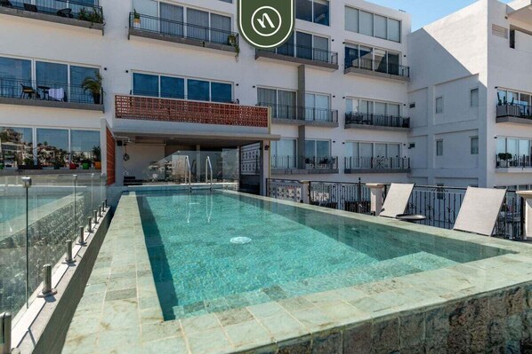 A rooftop swimming pool with clear water, surrounded by a glass barrier.