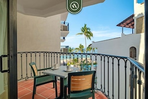 A balcony with a table and chairs, a view of the beach, and a palm tree.