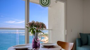 A dining table with plates and cutlery, a vase with flowers, and a view of the ocean and beach through a balcony door.