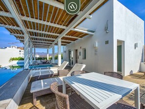 Un espace piscine sur le toit, avec des chaises longues et une table, un patio couvert doté d’un plafond en bois, et une vue sur les montagnes en arrière-plan.