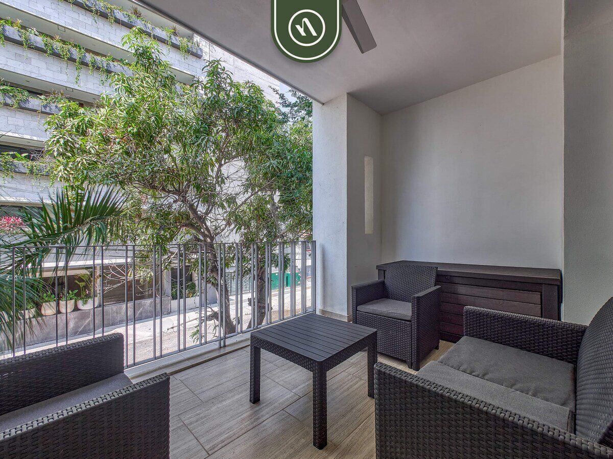 A balcony with wicker furniture, a small table, and a view of a street and greenery.