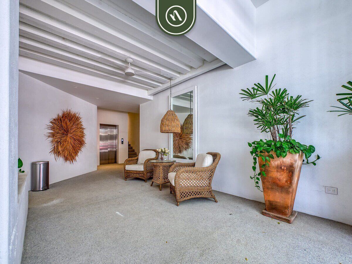 A spacious hallway with wicker furniture, a large potted plant, and a mirror reflecting the room.