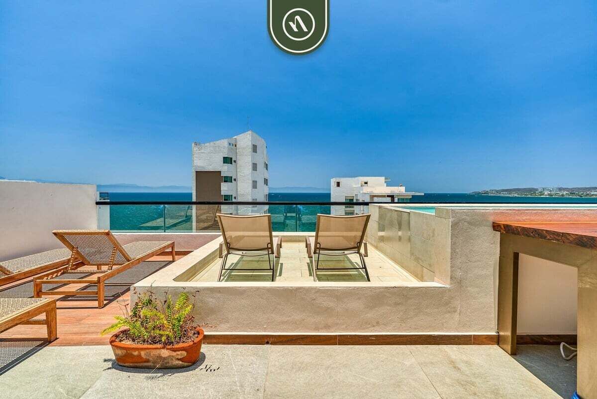A rooftop terrace with a pool, two lounge chairs, and a potted plant.