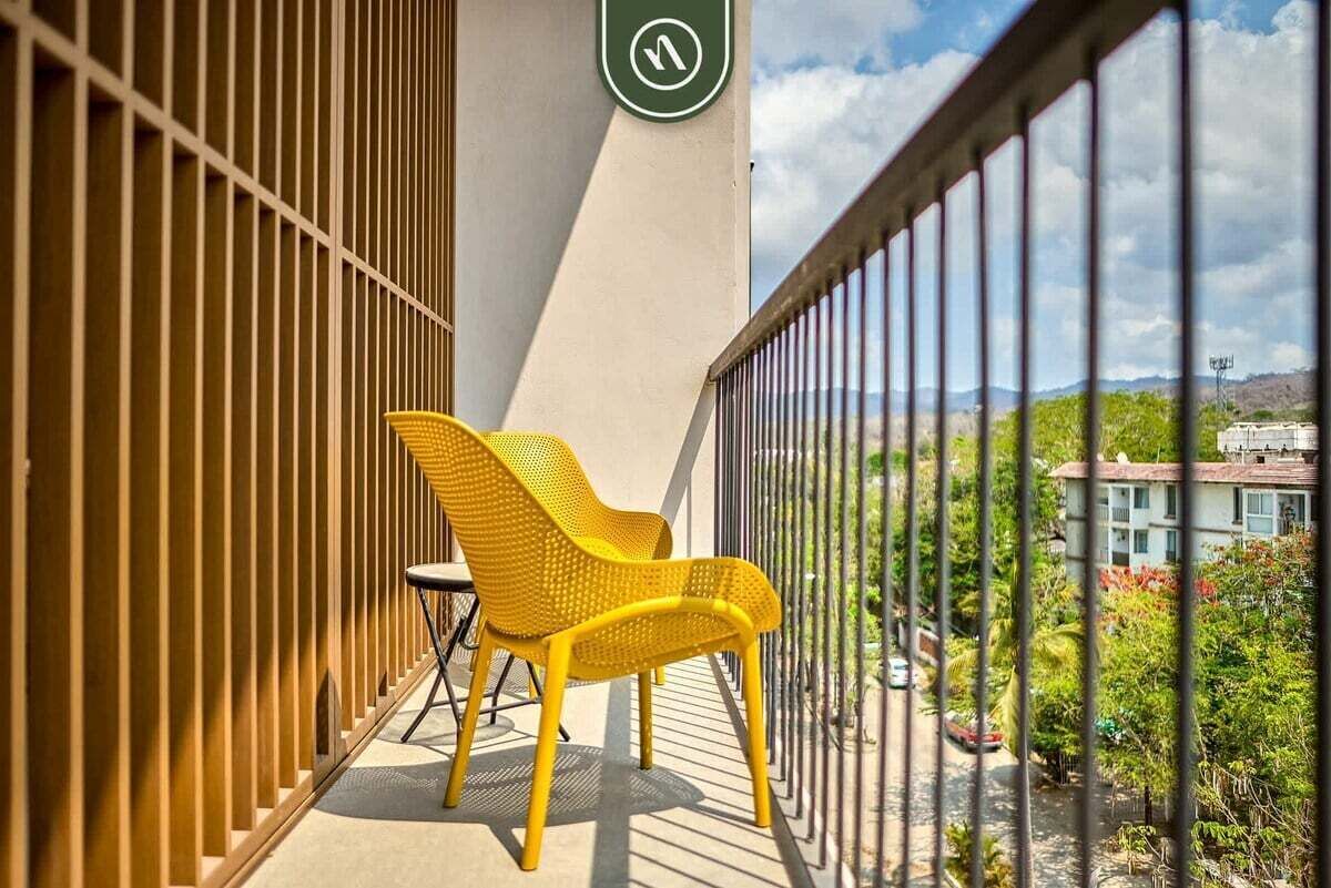 A balcony with yellow chairs, a green sign, and a view of a residential area.