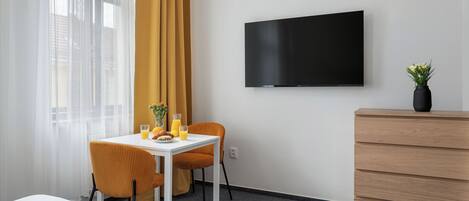 Una habitación de hotel con cama, una mesa con alimentos para el desayuno, un televisor y un aparador de madera.