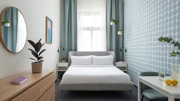 A hotel room with a bed, bedside tables, a desk, a chair, a mirror, and a potted plant.