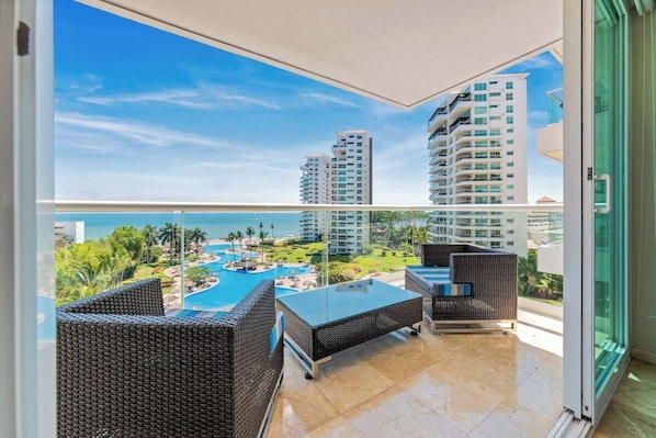 A balcony with wicker furniture, a glass door, and a view of a pool and high-rise buildings.