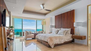 Une chambre moderne avec un grand lit, un ventilateur de plafond, une vue sur l’océan et un mur d’accent en bois.