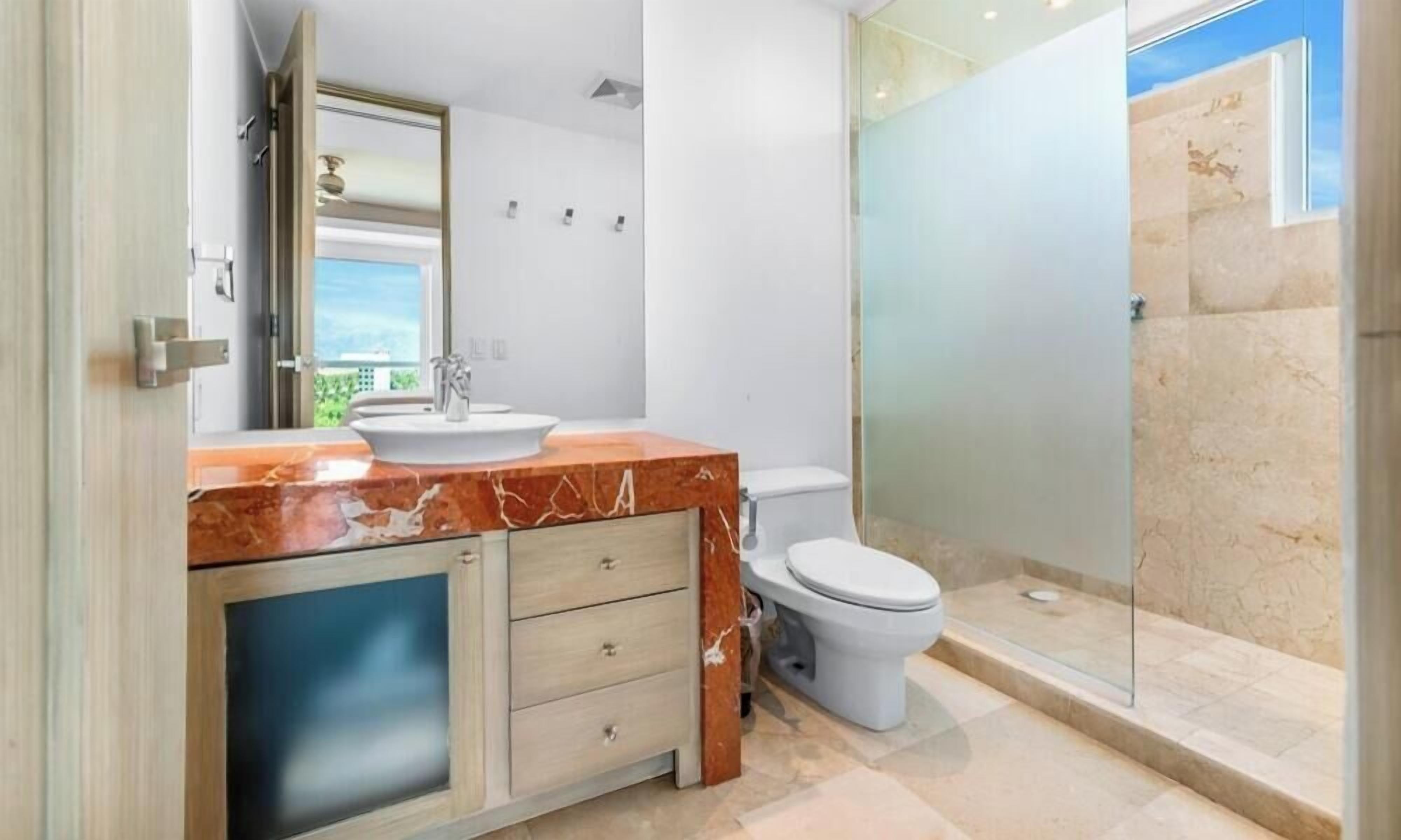 A bathroom with a marble vanity, a toilet, and a glass shower enclosure.