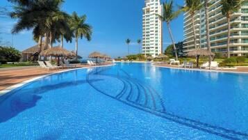 A swimming pool with lounge chairs, palm trees, and a tall hotel building.
