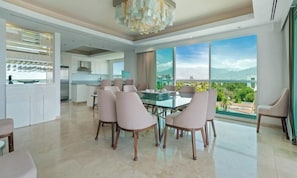 Un comedor moderno con una mesa y sillas de vidrio, una cocina al fondo y un ventanal con vista a la ciudad.
