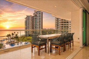 A balcony with a table and chairs overlooking a swimming pool and high-rise buildings during sunset. - Shangri-La Puerto Vallarta 4BR | Beachfront, Ocean Views, Heated Pool & Hot Tub (Puerto Vallarta)