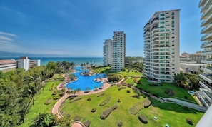 A resort with a central swimming pool, high-rise buildings, and a clear view of the ocean.