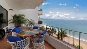 Een balkon met een tafel en stoelen, met uitzicht op een strand en de oceaan.