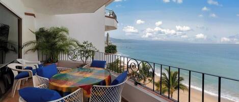 Ein Balkon mit Tisch und Stühlen mit Blick auf Strand und Meer.