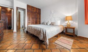A bedroom with a bed, wooden wardrobe, a nightstand with a lamp, and a patterned rug.