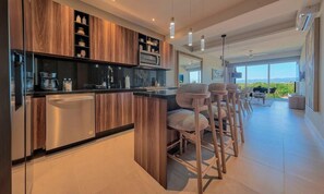 Cozinha moderna com armários de madeira, geladeira de aço inoxidável e um espaço bar com banquetas.