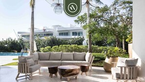 A modern outdoor seating area with a sofa, chairs, and coffee tables, overlooking a pool and a building. - New 2BR APT - Beach Access - Pool - GYM - Jacuzzi (Nuevo Vallarta)