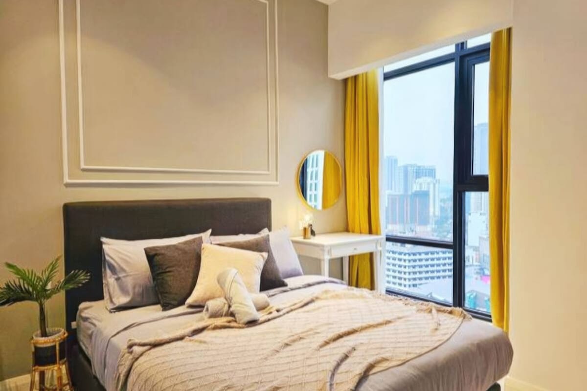 Quarto de hotel com uma cama grande, mesa de cabeceira, espelho e janela com cortinas.