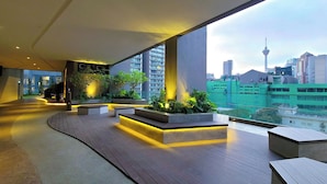 A modern outdoor area with wooden flooring, built-in planters with greenery, and a view of a cityscape including a tower. - Axon Residence by Emily in Town (Kuala Lumpur)