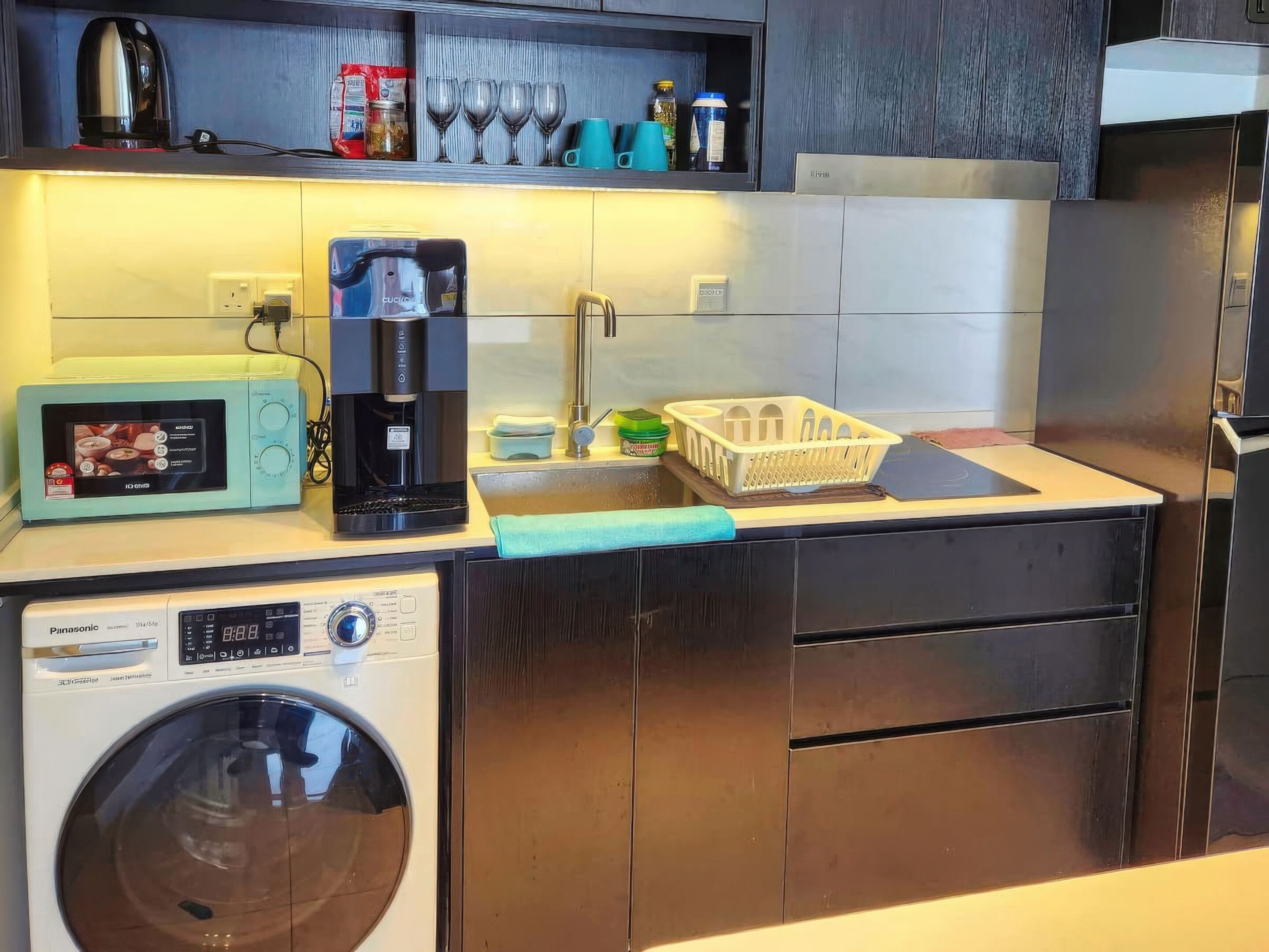 Une cuisine compacte équipée d’un lave-linge, d’une machine à café et d’un four à micro-ondes.