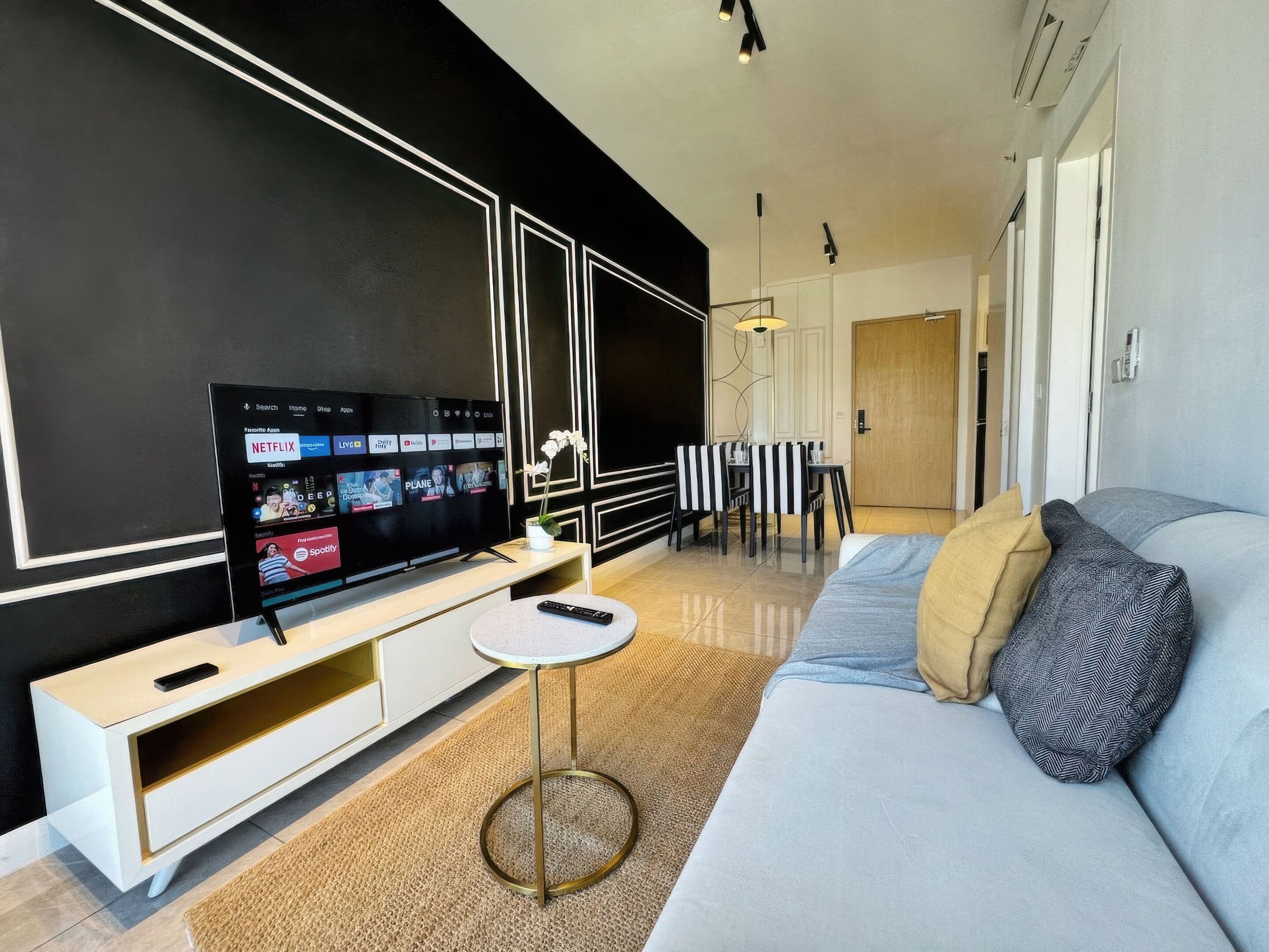 Una sala moderna con un televisor de pantalla plana grande, un sofá, una mesa de centro y un comedor con mantel a rayas.