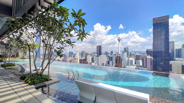 A rooftop infinity pool with a city skyline view, surrounded by trees and modern buildings. - Axon Residence by Emily in Town (Kuala Lumpur)