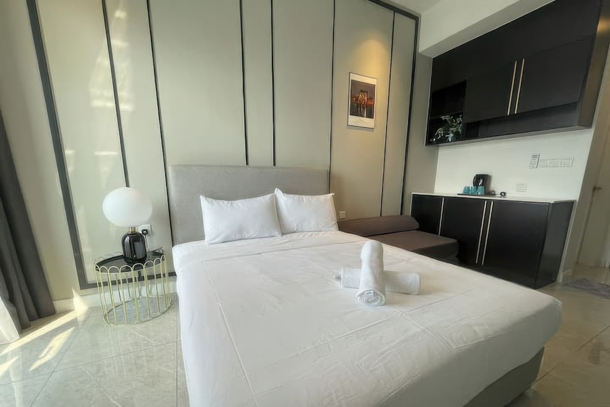 Quarto de hotel moderno com uma cama grande, mesa de cabeceira, escrivaninha e guarda-roupa.