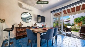 A dining area with a wooden table, blue chairs, and a TV mounted on the wall. - Cozy 3BR House Perfect for Families - Pool (Nuevo Vallarta)