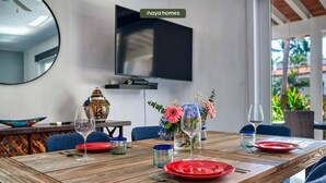 A dining area with a wooden table set for four, a television mounted on the wall, and a view of the outdoors. - Cozy 3BR House Perfect for Families - Pool (Nuevo Vallarta)